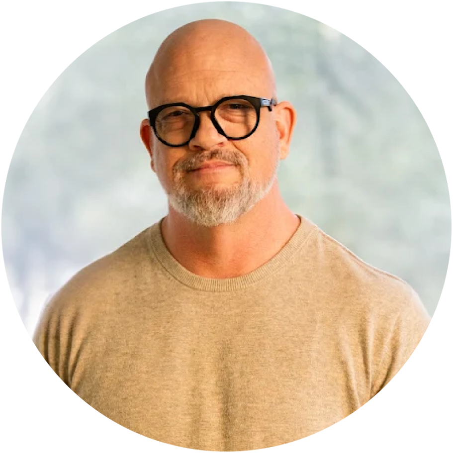 Bald man with a gray beard and black glasses, wearing a beige sweater, looking at the camera.